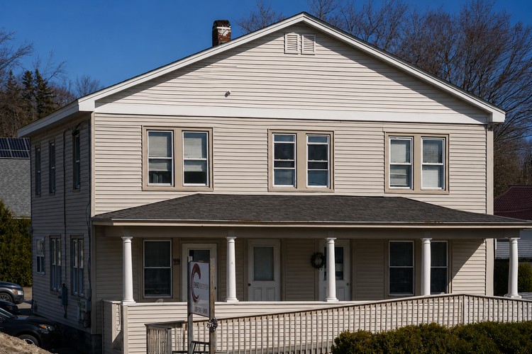 Cream clapboard two-story Augusta clinic building with wraparound porch under a clear blue spring sky