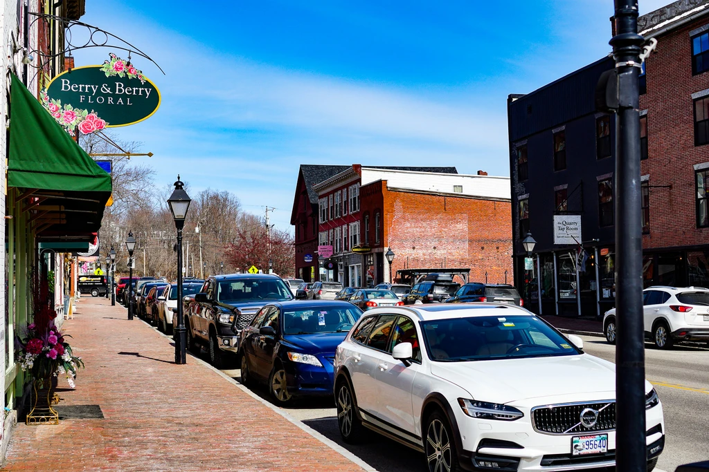 A quiet tree-lined residential street in a Maine town conveying a grounded sense of community living and everyday normalcy.